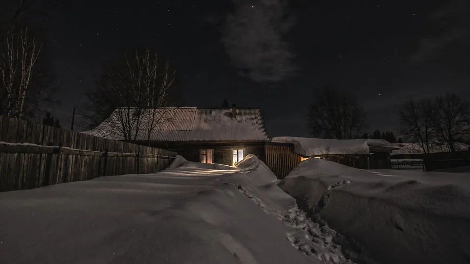 Sniega kupenas un iestaigāta taka pie mājas ziemas naktī